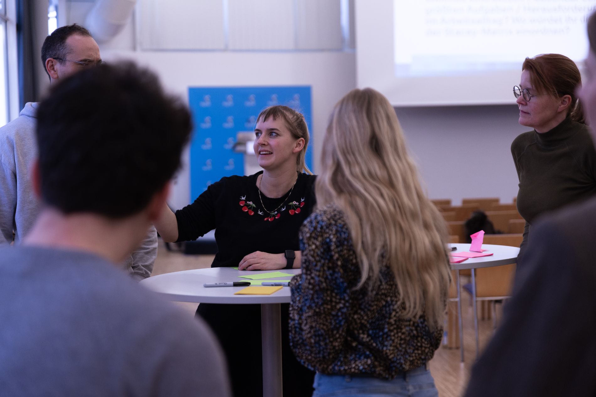 Eine Mitarbeiterin der byte steht zum Publikum gerichtet an einem Stehtisch und erklärt 4 Kollegen und Kolleginnen etwas